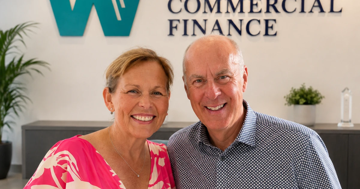 Two smiling people seated in front of a wall displaying Winning Commercial Finance logo