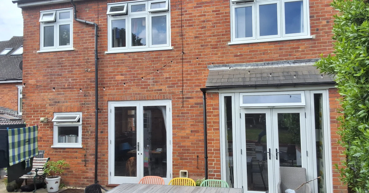 Rear view of a brick period house with new white Residence Collection windows and double doors opening to a patio with multicolored chairs