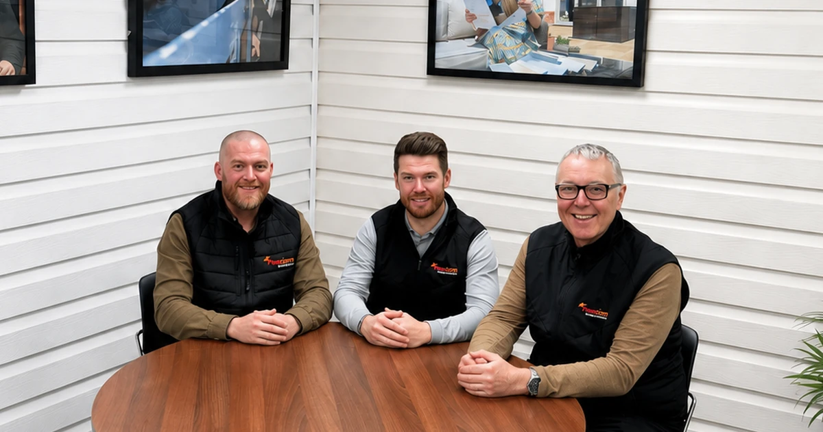 Three men sitting around a wooden table wearing Freefoam branded black vests in a white panelled room with framed photos on the walls