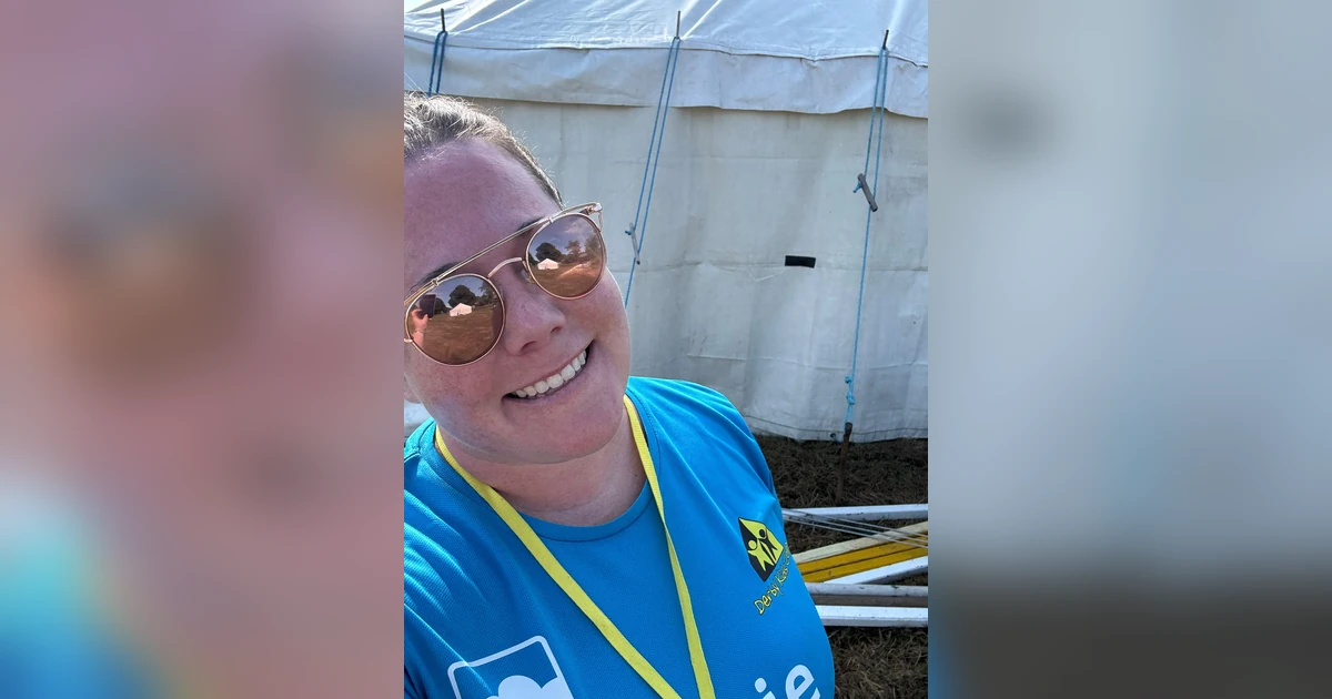Katie Bregazzi smiling wearing sunglasses and a Derby Kids' Camp blue shirt standing in front of a large white tent