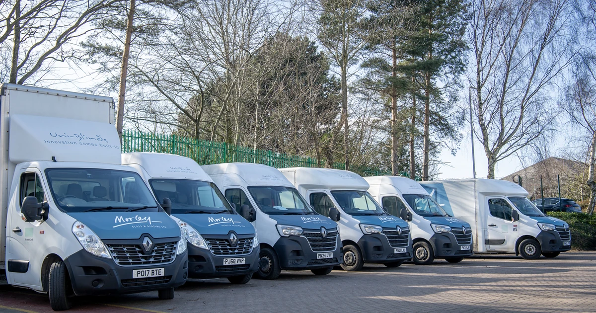 Row of Morley Glass delivery vans parked outdoors with trees in background