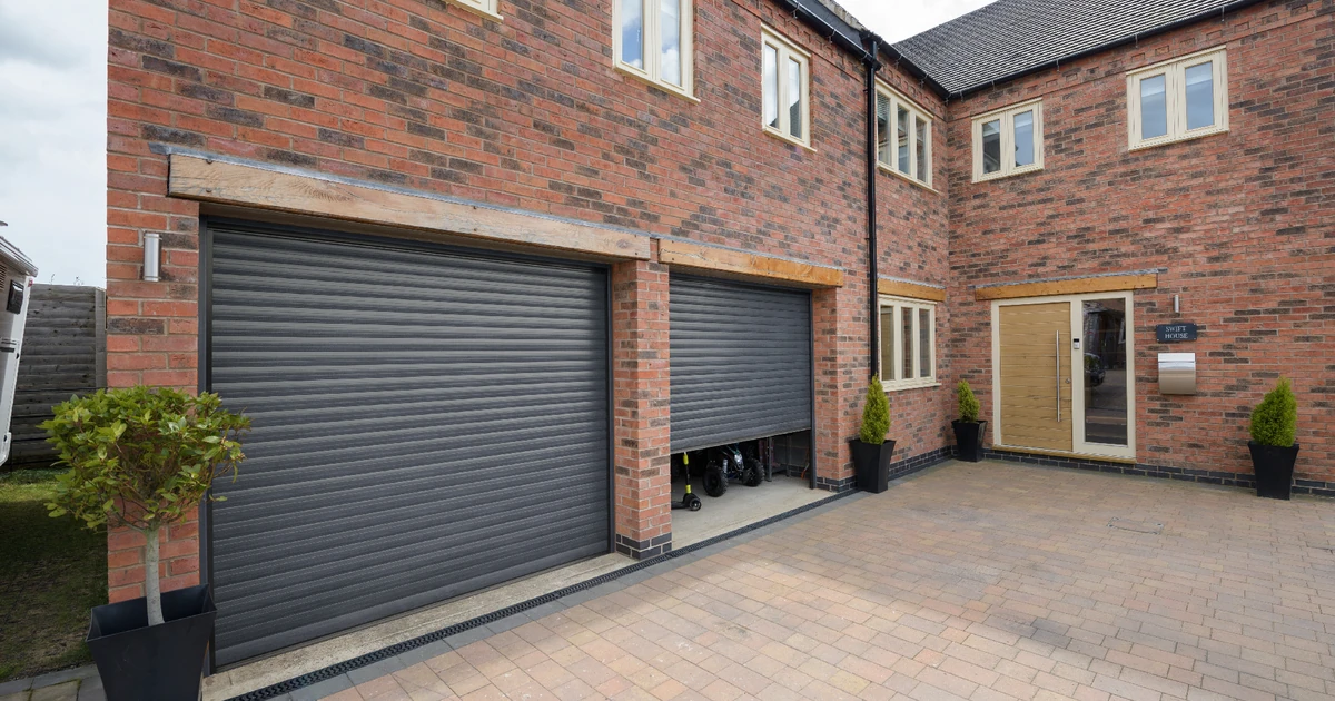 Anthracite-colored roller garage doors installed on a modern brick residential building with paved driveway