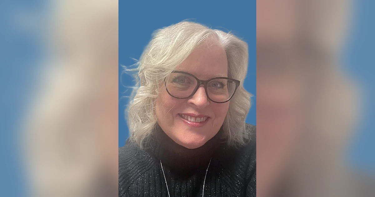 Smiling woman with glasses and gray hair against blue background