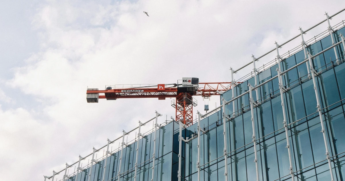 Glass and aluminium cladding on modern building under construction with a large red crane overhead against a blue sky