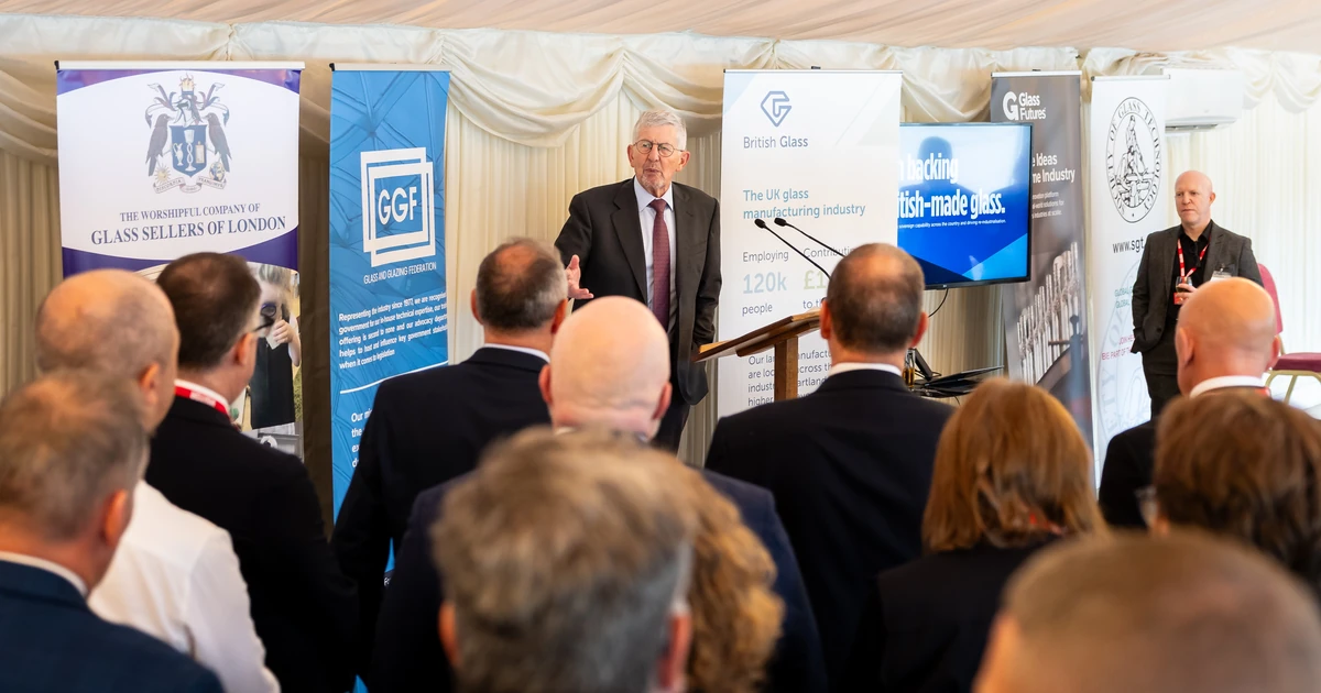 Man speaking at a podium during the Glass & Glazing Federation event with banners in the background