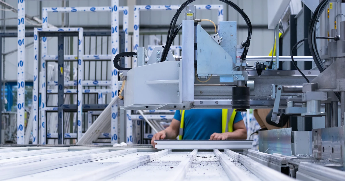 Worker operating large fabrication machinery in a factory setting producing window and door frames