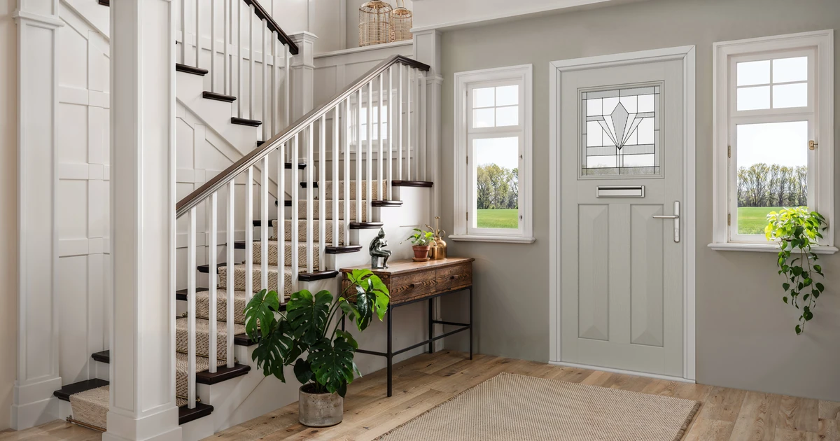 Solid timber core front entrance door with decorative glass panel set in a bright home interior hallway with staircase and plants