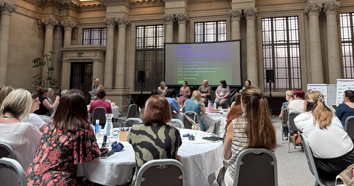 Women attending a Women in Fenestration Network event seated around tables, panelists speaking on stage in a large hall with high decorative ceilings