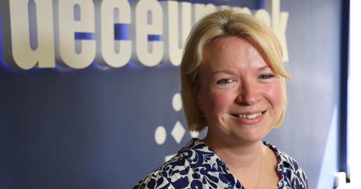 Smiling woman standing in front of a blue wall with the Deceuninck logo