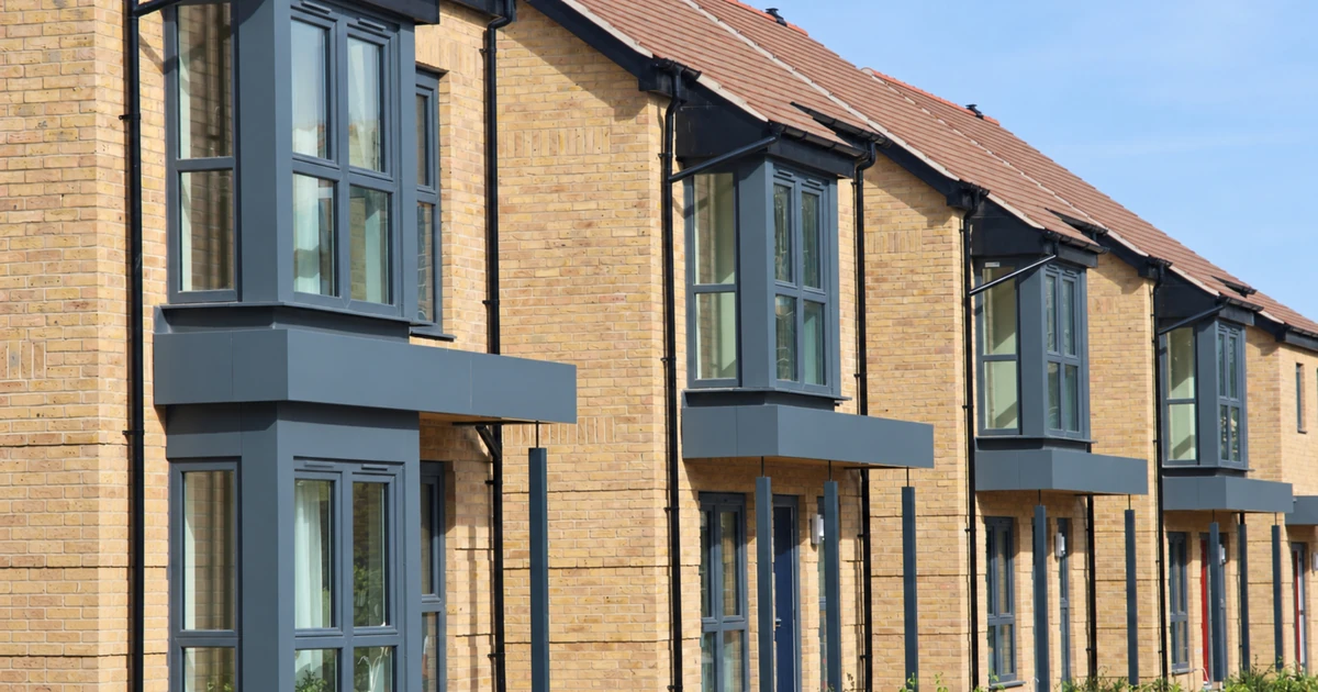 Row of modern social housing homes featuring multiple energy efficient grey framed windows under clear sky
