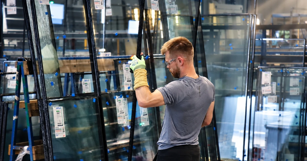 Worker in factory handling glazed window units surrounded by glass panels