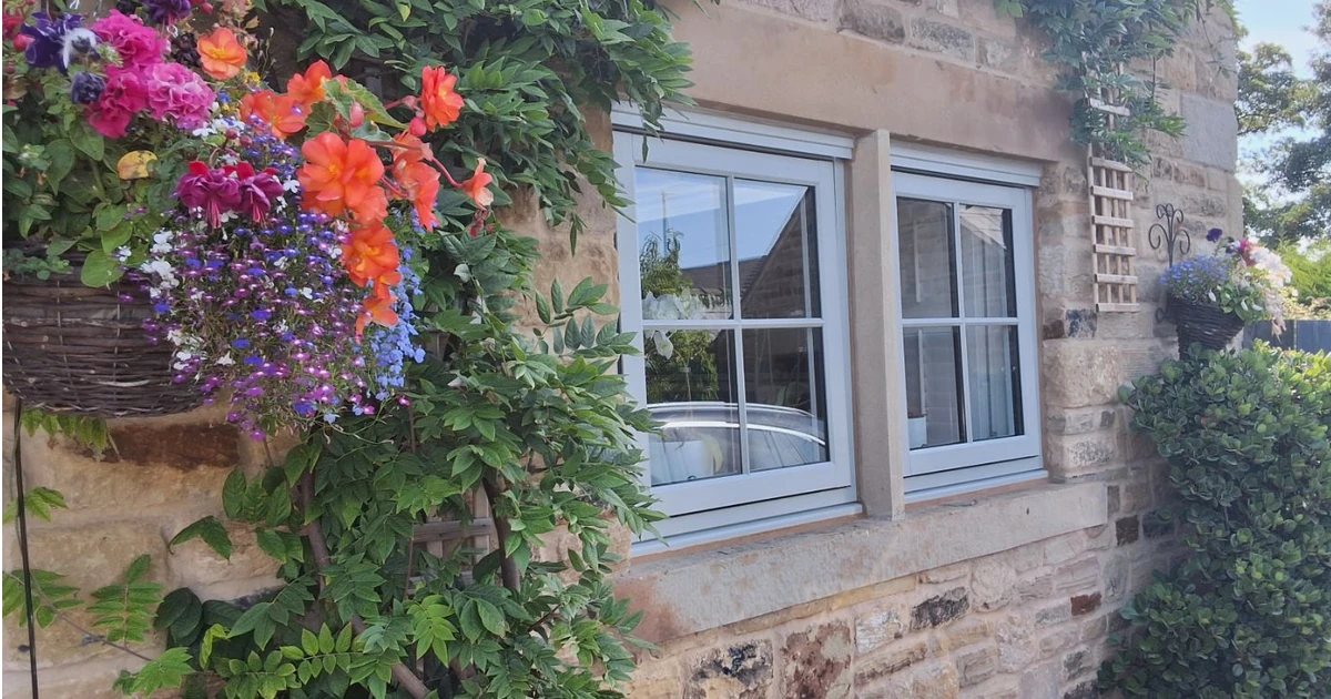 Close-up of two windows in a stone wall with colorful flowers and green plants around