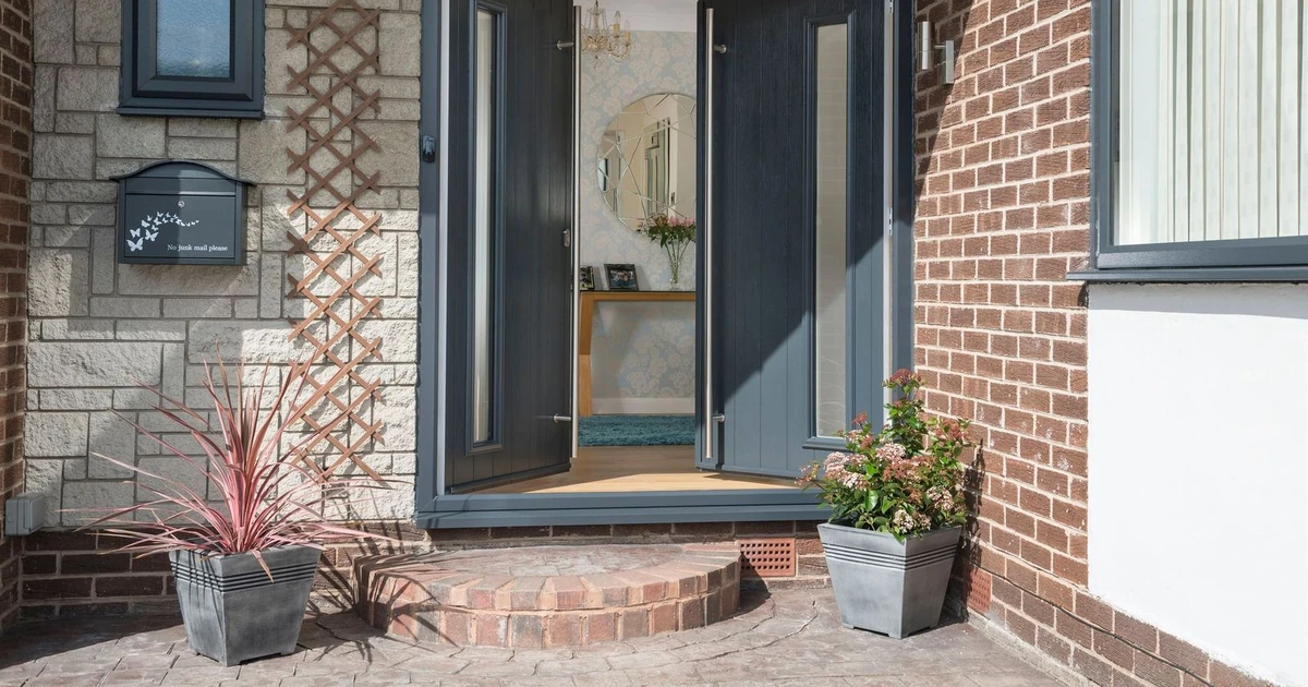 Blue composite entrance door open at residential home entrance with brick and stone walls and potted plants outside