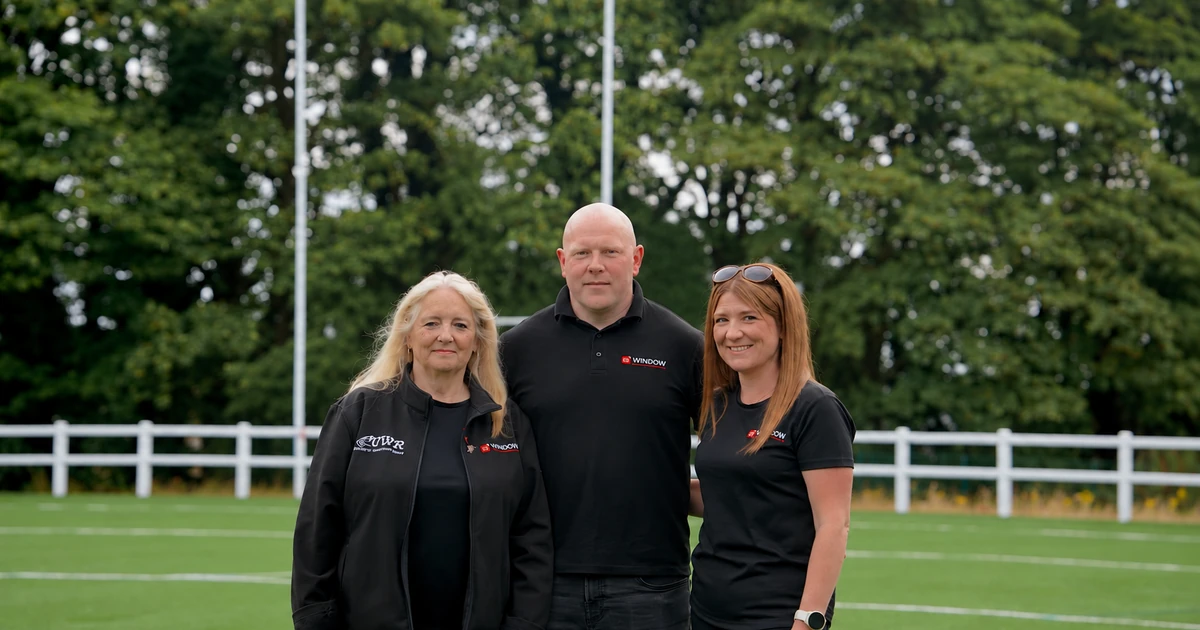 Three people standing on a grassy field with trees in the background, wearing Window Control Systems branded clothing.