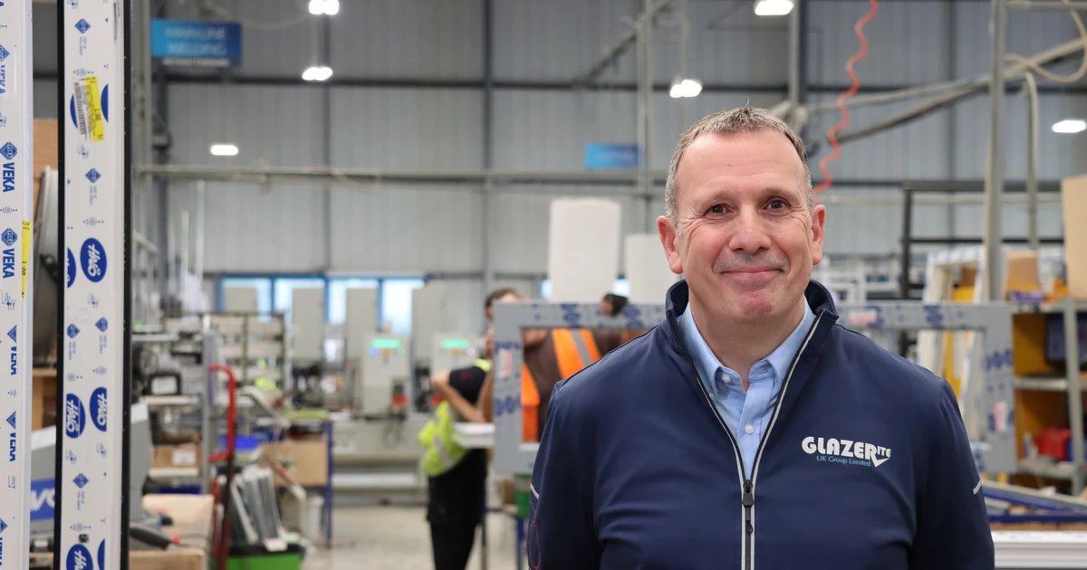 Man wearing a Glazerite jacket standing inside a factory with production equipment in the background
