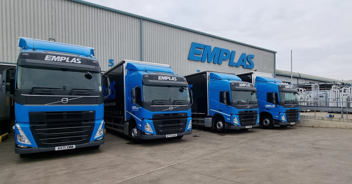 Four blue Emplas delivery trucks parked outside a large Emplas depot building under a dull sky