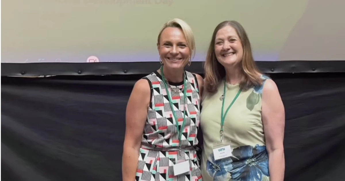 Sioned Yates and Sarah Ball standing in front of a screen showing the WFN logo, smiling at an event